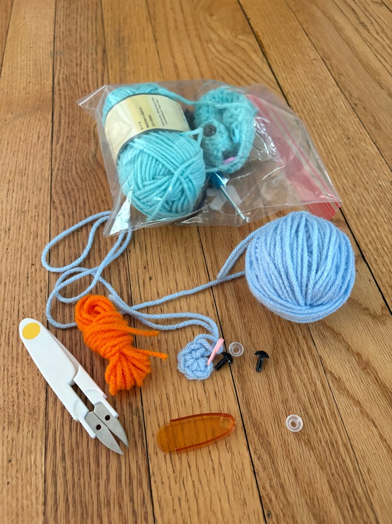 Yarn, safety eyes, crochet hook, scissors, and all the necessary materials are laid out on floor.